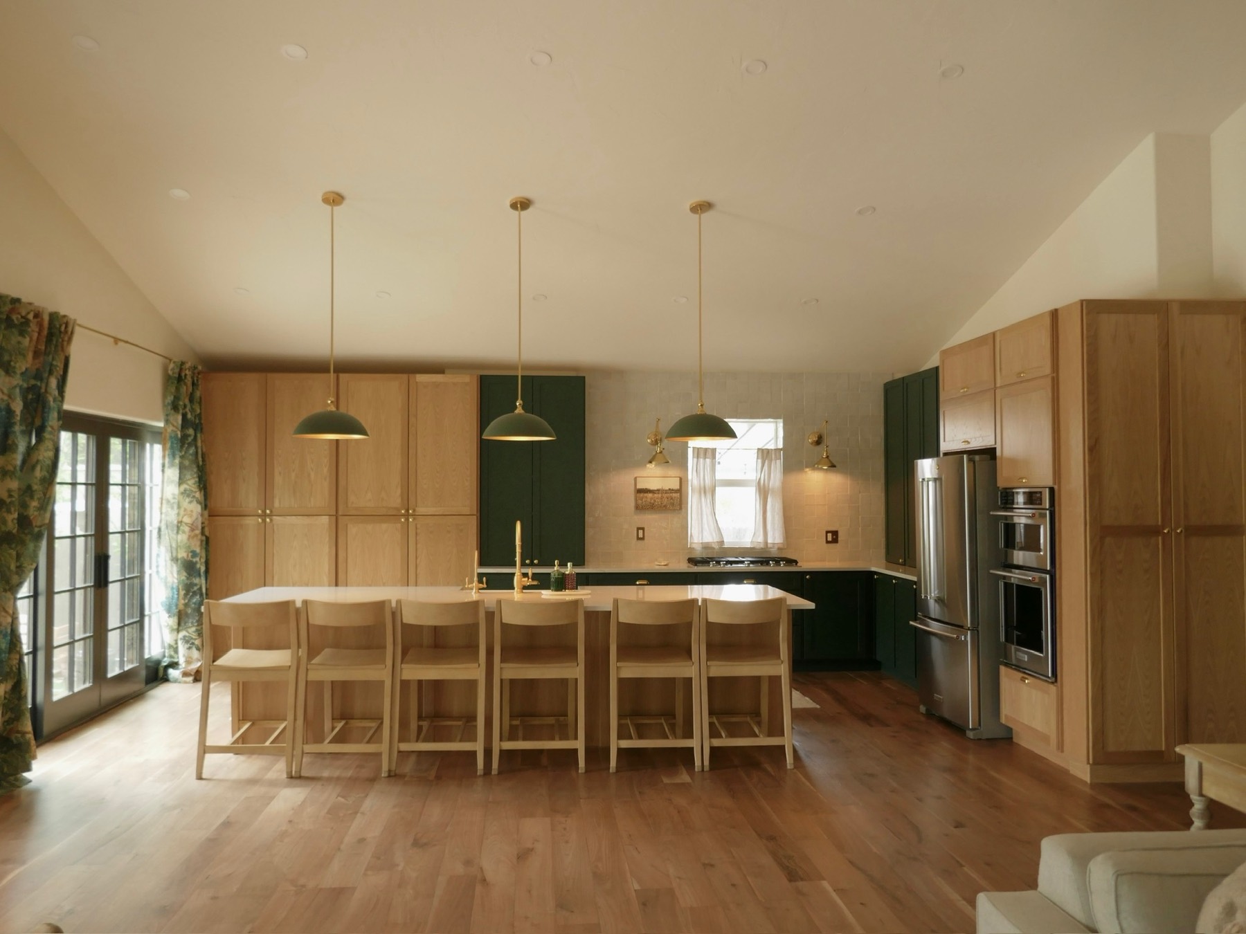 The kitchen after the remodel — white oak cabinetry, green accents, and brass pendants