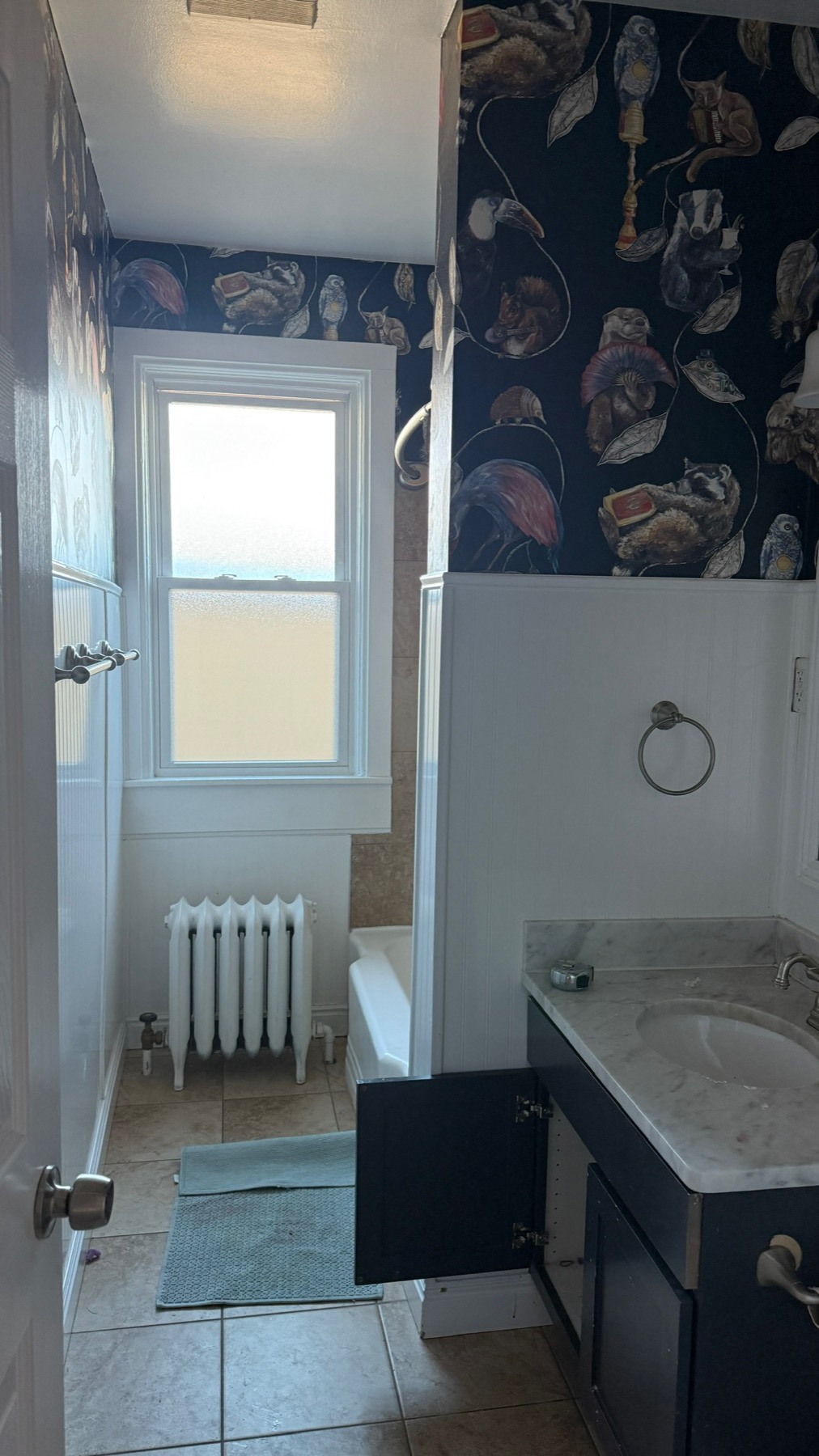 The bird-wallpaper bath before the remodel — beige tile tub and dated fixtures